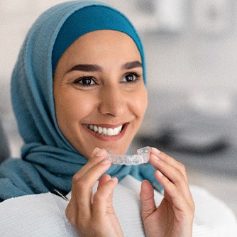 Woman smiling while holding Invisalign aligner