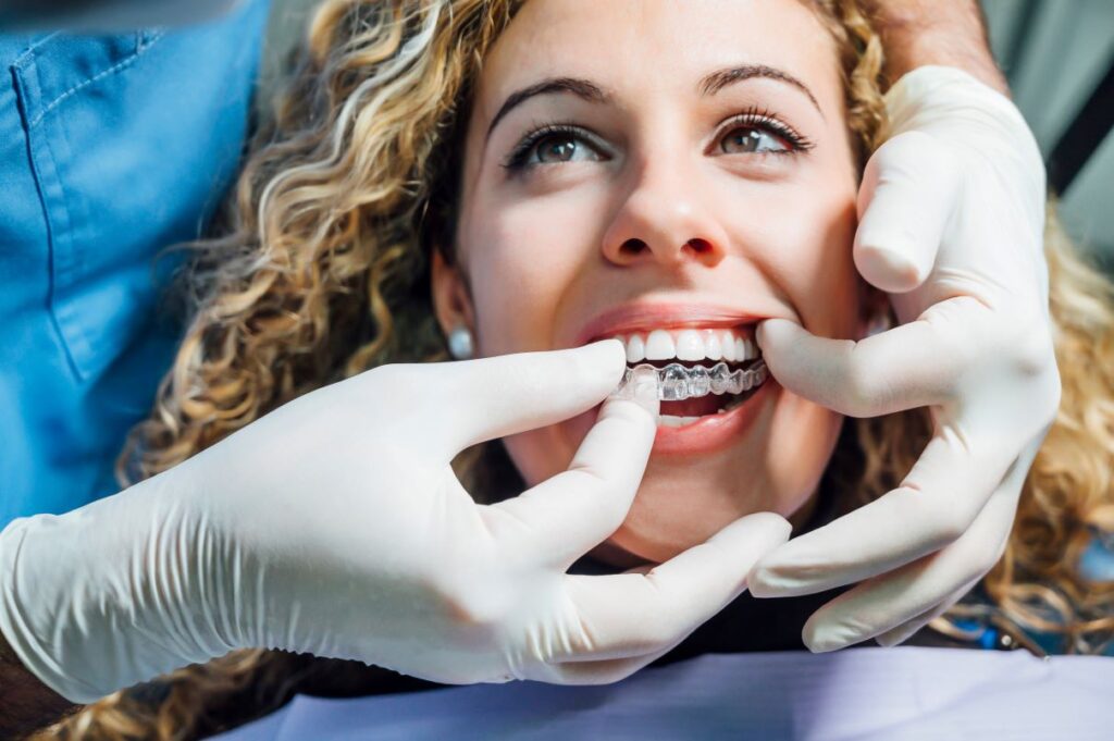 A dentist helping a woman put on an Invisalign aligner.