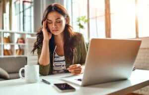 Woman sitting at her desk, struggling with a migraine